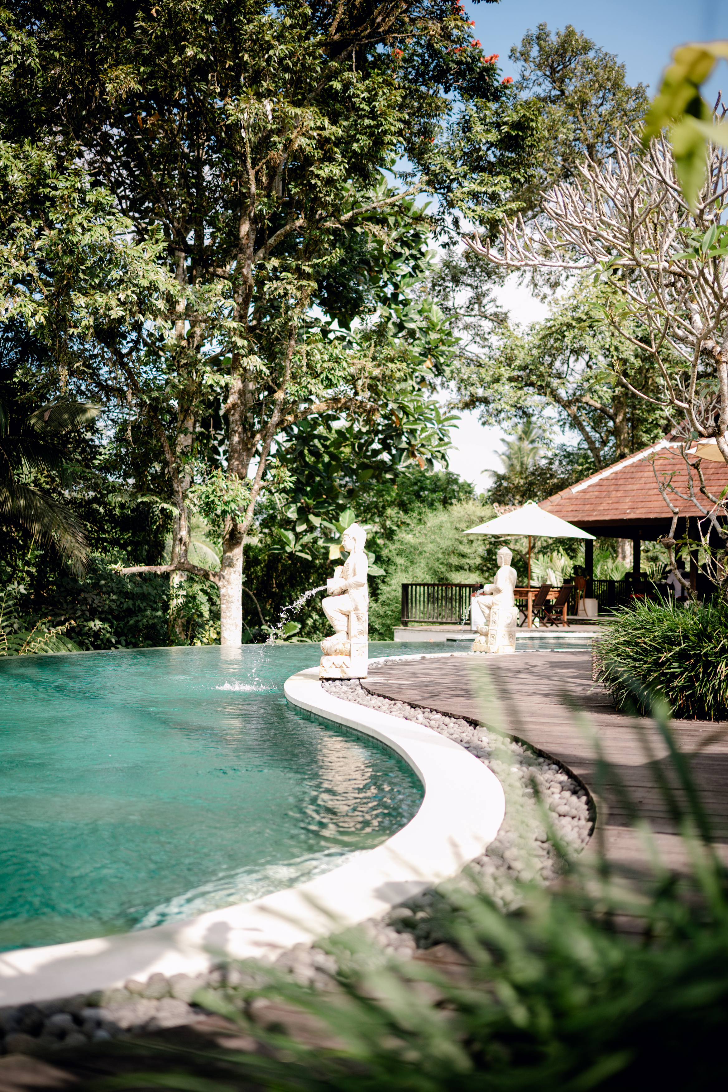 Infinity pool with Balinese stone statues surrounded by rainforest at BeingSattvaa